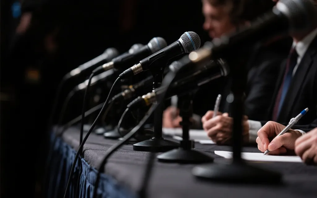 发布会麦克风与记者记录本特写，象征舆论与叙事的交锋